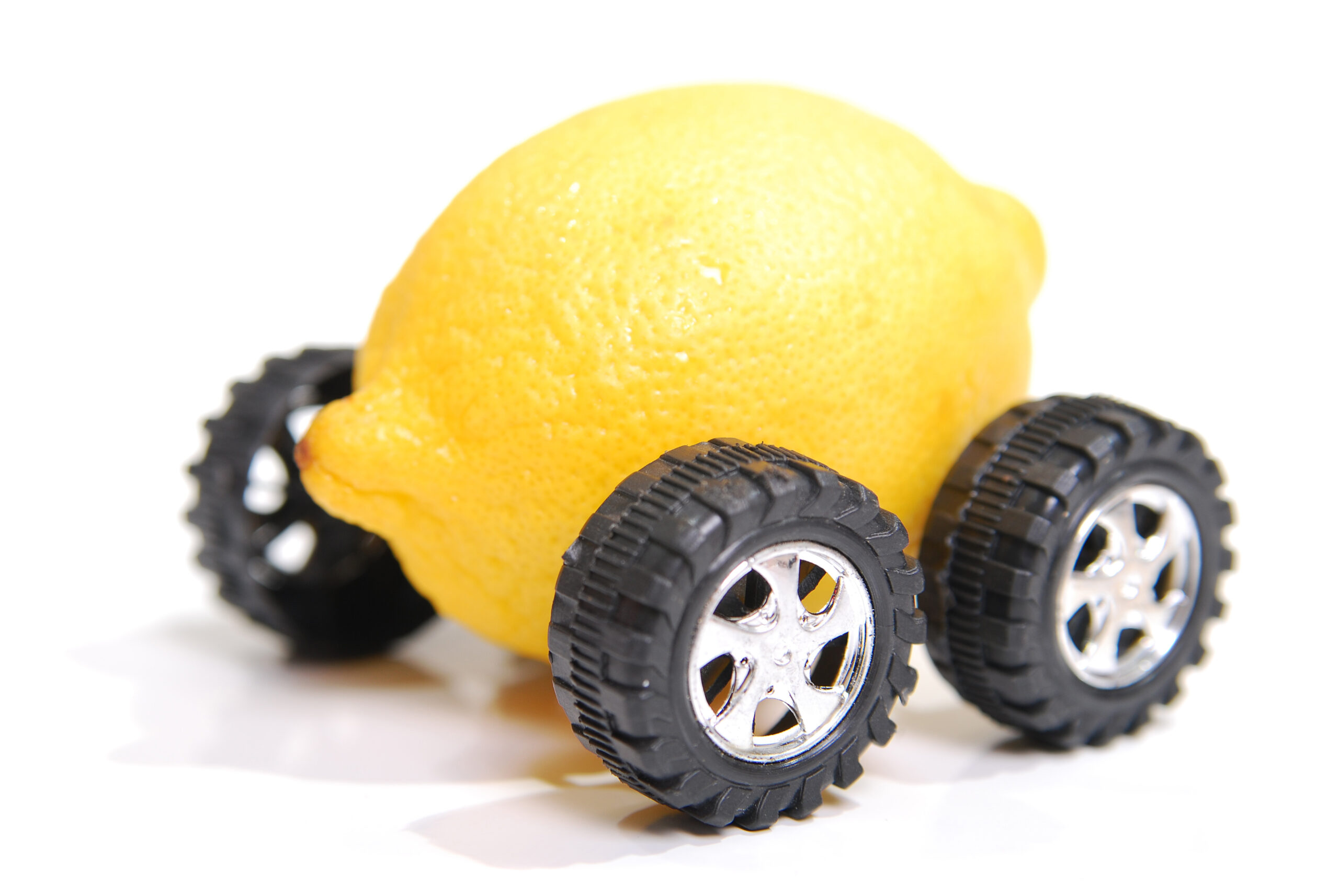 A lemon with wheels representing a defective vehicle. Shallow depth of field focus on fron wheel and front of lemon.